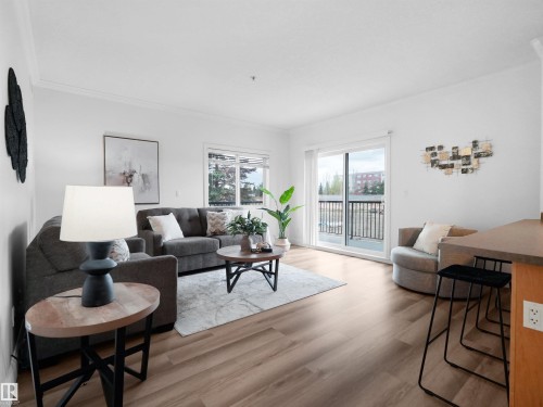 Living area featuring wood-finish flooring, white walls, and a sliding glass door opening to a private balcony with black railings - 104 14612 125 Street, Edmonton, AB 