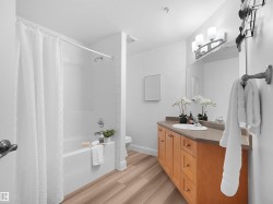 Full bathroom featuring a tub/shower combination with white subway tile surround, wood-finish flooring, and a vanity with light wood cabinetry and a neutral countertop - 