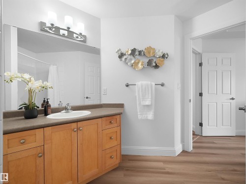 Bathroom vanity with light wood-finish cabinetry, a large integrated mirror, and a sleek vanity light fixture - 104 14612 125 Street, Edmonton, AB 