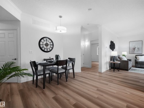 Open-concept living space featuring wood-finish flooring, white baseboards, and crown molding - 104 14612 125 Street, Edmonton, AB 