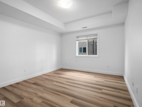 Spacious room featuring wood-finish flooring, white baseboards, and bright white walls - 104 14612 125 Street, Edmonton, AB 