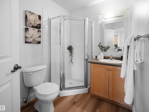 Three-piece bathroom featuring a corner shower with glass enclosure, a vanity with wood-finish cabinetry and integrated sink, and wood-finish flooring - 104 14612 125 Street, Edmonton, AB 