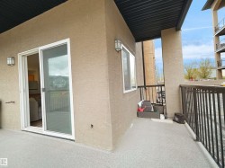 Private balcony featuring a textured stucco exterior, white-framed sliding glass door, and a black metal railing - 