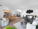 Open-concept living space featuring wood-finish flooring, a kitchen with light wood cabinetry and stainless steel appliances, and a breakfast bar - 104 14612 125 Street, Edmonton, AB 