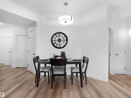 Dining area featuring wood-finish flooring, crisp white walls, crown molding, a modern ceiling light fixture, and white interior doors - 104 14612 125 Street, Edmonton, AB 