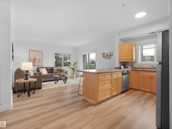 Open-concept living space featuring wood-finish flooring, a kitchen island with seating, natural wood cabinetry, and a sliding glass door leading to an outdoor area - 