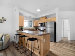 Kitchen featuring light wood cabinetry, stainless steel appliances, a breakfast bar, and wood-finish flooring - 