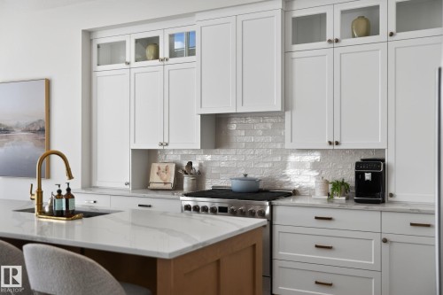 Kitchen featuring white shaker-style cabinetry, a white subway tile backsplash, a gold-finish faucet, a stainless steel range, and stone countertops - 14 Jane Point(E), St. Albert, AB 
