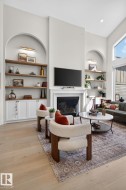 Bright living area featuring a tall fireplace with a white mantel, arched built-in shelving with accent lighting, white cabinetry, and wood-finish flooring - 