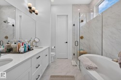 Spacious bathroom featuring a freestanding soaking tub, a frameless glass shower enclosure, a dual vanity with undermount sinks, and a large privacy window - 