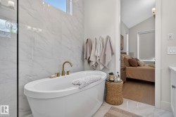 Freestanding soaking tub with gold-finish fixtures and floor-to-ceiling marbled tile surround - 