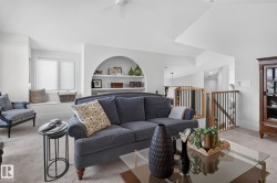 Carpeted living area featuring a built-in arched shelving unit, a window seat with roller shades, and a ceiling fan - 