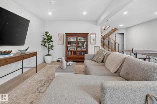 Spacious recreational room featuring wood-finish flooring, recessed lighting, a built-in wooden bookcase, and a visible wooden staircase with natural wood railings - 14 Jane Point(E), St. Albert, AB 