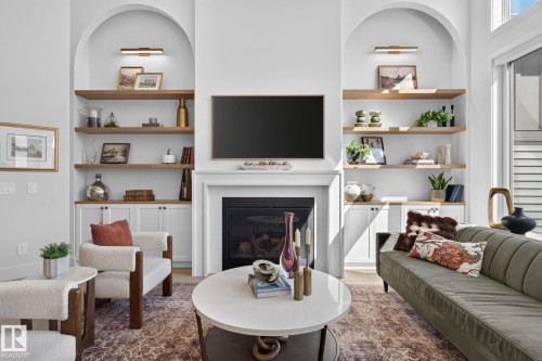 Living area featuring a fireplace with a white mantel, built-in shelving, arched wall niches, and wood-finish floating shelves with integrated lighting - 14 Jane Point(E), St. Albert, AB 