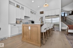 Contemporary kitchen featuring a light wood-finish island with seating, white shaker cabinetry, stainless steel appliances, and a vaulted ceiling - 