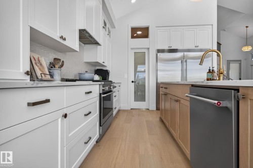 Bright kitchen featuring white shaker cabinetry, stainless steel appliances, a brass-finish faucet, light wood-finish flooring, and a glass-paneled pantry door - 14 Jane Point(E), St. Albert, AB 