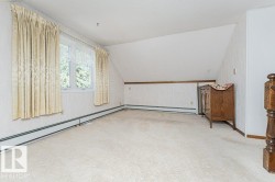 Spacious carpeted room featuring a white window with curtain rods, baseboard heating, and textured wallpaper - 