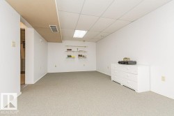 Spacious room featuring light-colored carpeting, white walls, and a drop ceiling with recessed lighting - 