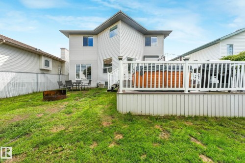 Rear exterior featuring light-colored siding, a raised deck with white railing, and a wood-paneled hot tub - 98 Bridgeport Wynd, Leduc, AB 