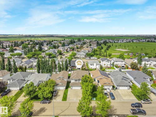 Aerial perspective showcasing a residential neighborhood with numerous single-family homes, mature trees, and expansive green spaces - 98 Bridgeport Wynd, Leduc, AB 