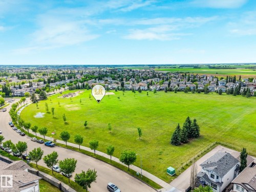 Expansive green space with manicured lawn and mature trees, surrounded by residential properties and a paved roadway - 98 Bridgeport Wynd, Leduc, AB 