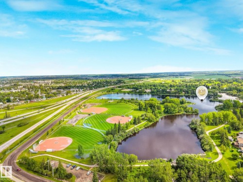 Aerial perspective showcasing multiple sports fields, a highway, and a body of water surrounded by lush greenery - 98 Bridgeport Wynd, Leduc, AB 