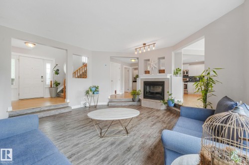 Spacious living area featuring wood-finish flooring, a corner fireplace with a light-toned surround, recessed display niches, and track lighting - 98 Bridgeport Wynd, Leduc, AB 