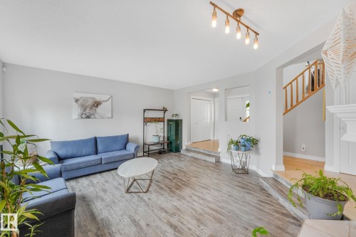 Spacious living area featuring wood-finish flooring, light gray walls, a multi-bulb track lighting fixture, and a staircase with natural wood railings - 98 Bridgeport Wynd, Leduc, AB 
