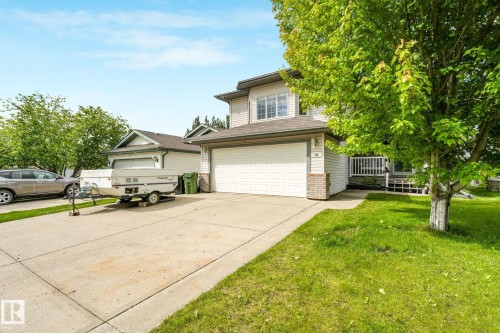 Two-story residence featuring light-colored siding, an attached garage with a white door, and a concrete driveway - 98 Bridgeport Wynd, Leduc, AB 