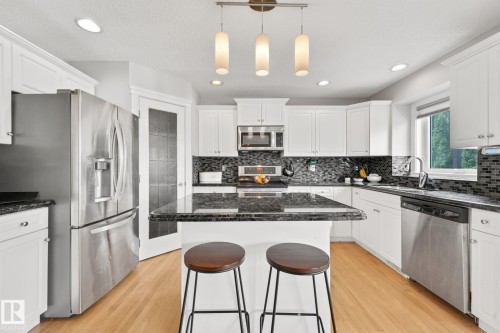Kitchen featuring white cabinetry, dark stone countertops, stainless steel appliances, wood-finish flooring, and recessed lighting - 98 Bridgeport Wynd, Leduc, AB 