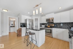 Kitchen featuring white cabinetry, dark stone countertops, stainless steel appliances, and a mosaic tile backsplash - 