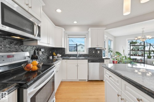 Kitchen featuring stainless steel appliances, white cabinetry, dark stone countertops, mosaic tile backsplash, and light wood-finish flooring - 98 Bridgeport Wynd, Leduc, AB 