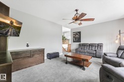 Carpeted living space featuring a ceiling fan with integrated lighting, light gray wall paint, and a wood-finish media console - 