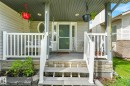 Covered front porch featuring white railings, a dark green entry door with a screen, and a porch swing - 98 Bridgeport Wynd, Leduc, AB 
