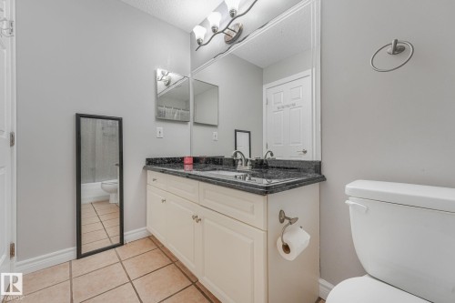Bathroom featuring a dual-sink vanity with a dark countertop and light-colored cabinetry, wall-mounted light fixture, and tile flooring - 98 Bridgeport Wynd, Leduc, AB 