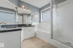 Bathroom featuring a dual vanity with dark countertops, white cabinetry, a built-in tub, and a glass-enclosed shower - 