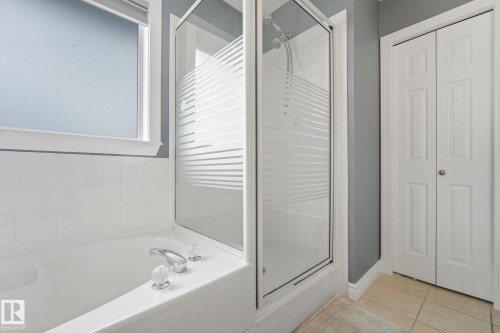 Bathroom featuring a shower-over-tub combination with clear and frosted glass enclosure, white ceramic wall tiling, a window with textured privacy glass, chrome fixtures, and neutral-toned floor tiles - 98 Bridgeport Wynd, Leduc, AB 