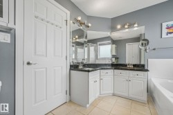 Bathroom vanity featuring dual sinks with dark stone countertops, white cabinetry, and large mirrors - 