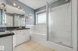 Bathroom featuring a glass-enclosed shower, a built-in jetted tub, a vanity with a dark countertop, an integrated sink, and white cabinetry - 