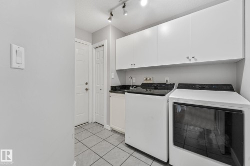 Laundry area featuring white cabinetry, dark countertop, and tile flooring - 98 Bridgeport Wynd, Leduc, AB 