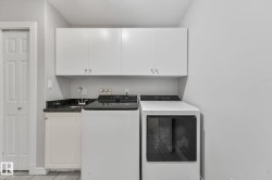 Dedicated laundry area featuring a utility sink with a stainless steel faucet, dark stone-finish countertop, and upper white cabinetry for storage - 