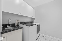 Utility room featuring a dark granite countertop with an undermount sink, white cabinetry, and white tile flooring - 