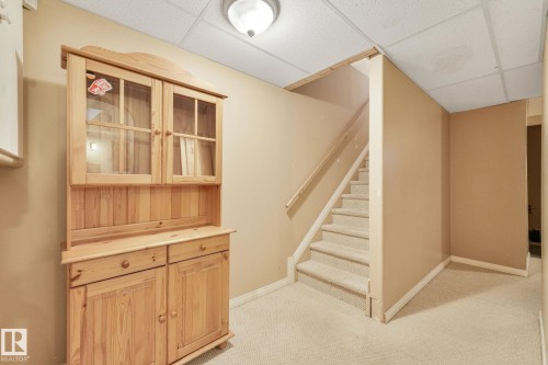Carpeted staircase with a wood handrail, beige wall paint, and a dropped ceiling - 98 Bridgeport Wynd, Leduc, AB 