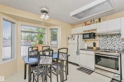 Kitchen featuring a bay window, white cabinetry, dark countertops, a patterned tile backsplash, and stainless steel appliances - 1612 80A Street, Edmonton, AB 