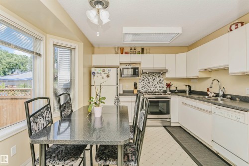 Kitchen featuring white cabinetry, dark countertops, a mosaic tile backsplash, and stainless steel appliances - 1612 80A Street, Edmonton, AB 