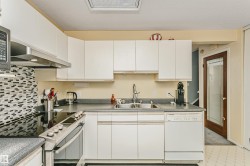 Kitchen featuring white cabinetry, a dual basin stainless steel sink, dark countertops, a mosaic tile backsplash, and a built-in dishwasher - 