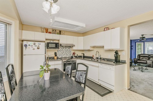 Bright kitchen featuring white cabinetry, a mosaic tile backsplash, and dark countertops - 1612 80A Street, Edmonton, AB 