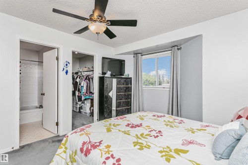 Interior room featuring a window with horizontal blinds, a ceiling fan with light fixture, gray carpeting, a walk-in closet, and a white tiled bathroom with a bathtub - 1612 80A Street, Edmonton, AB 