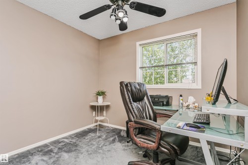Room featuring a window with exterior tree scenery, textured ceiling, a ceiling fan with light fixture, and neutral-toned wall paint - 1612 80A Street, Edmonton, AB 