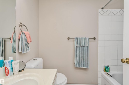 Bathroom featuring a white vanity with an integrated sink, a commode, and a shower-over-tub combination with white square tiles and a decorative border - 1612 80A Street, Edmonton, AB 